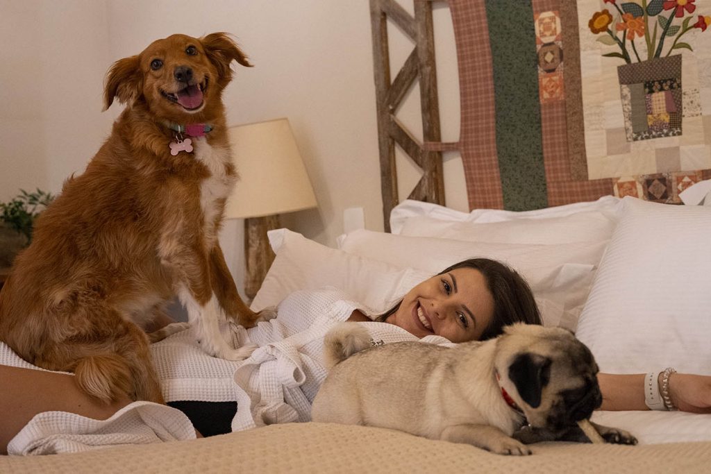 mulher sorrindo, com dois cachorros em cama de hotel em Gramado