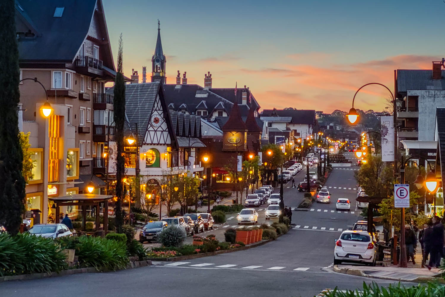 avenida com diversos estabelecimentos iluminados e céu do entardecer