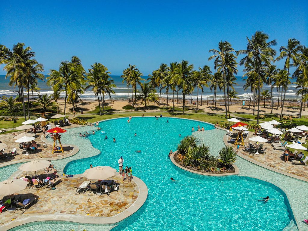 imagem de uma piscina de resort, com coqueiros e céu bem azul