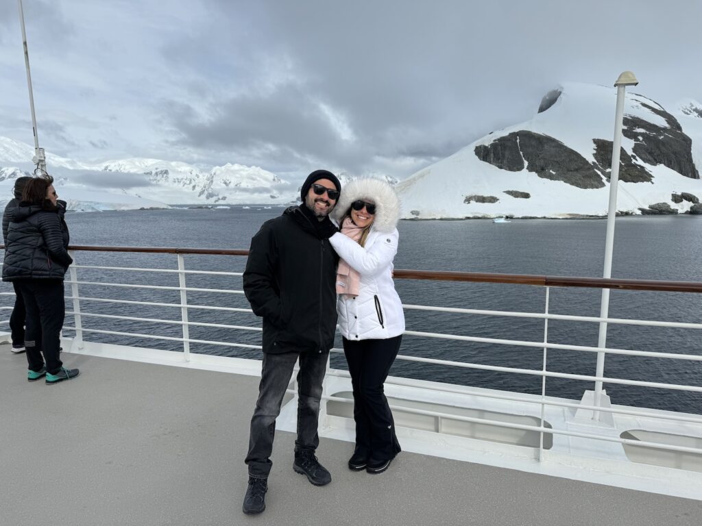casal fazendo selfie em frente a um iceberg, com dia ensolarado.