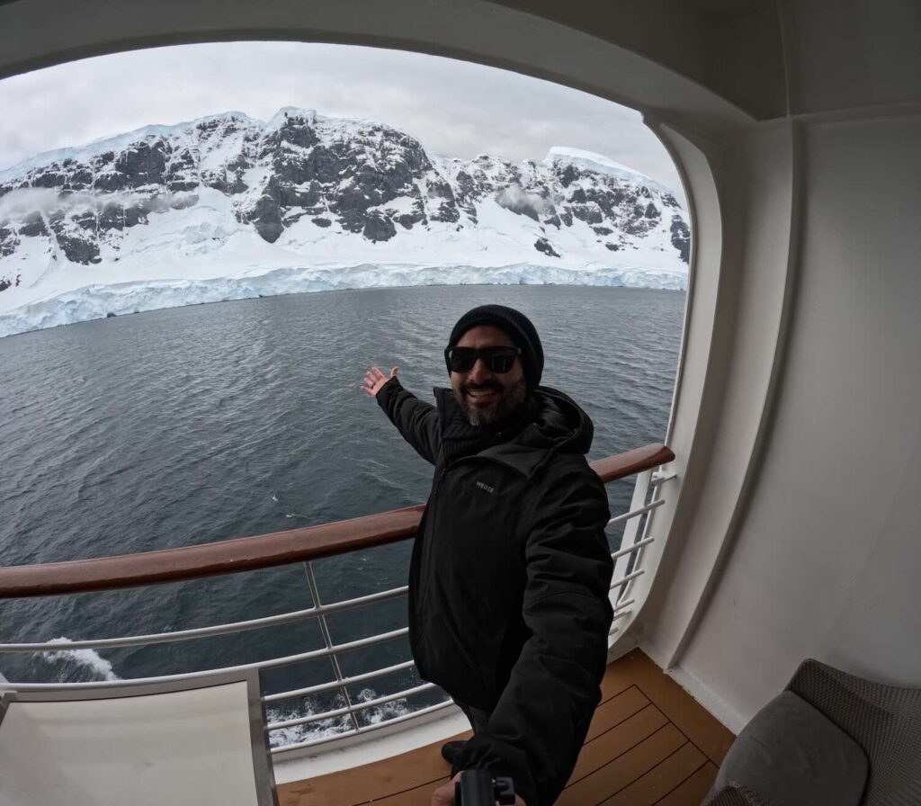 homem em sacada de um navio com geleiras da antártida ao fundo