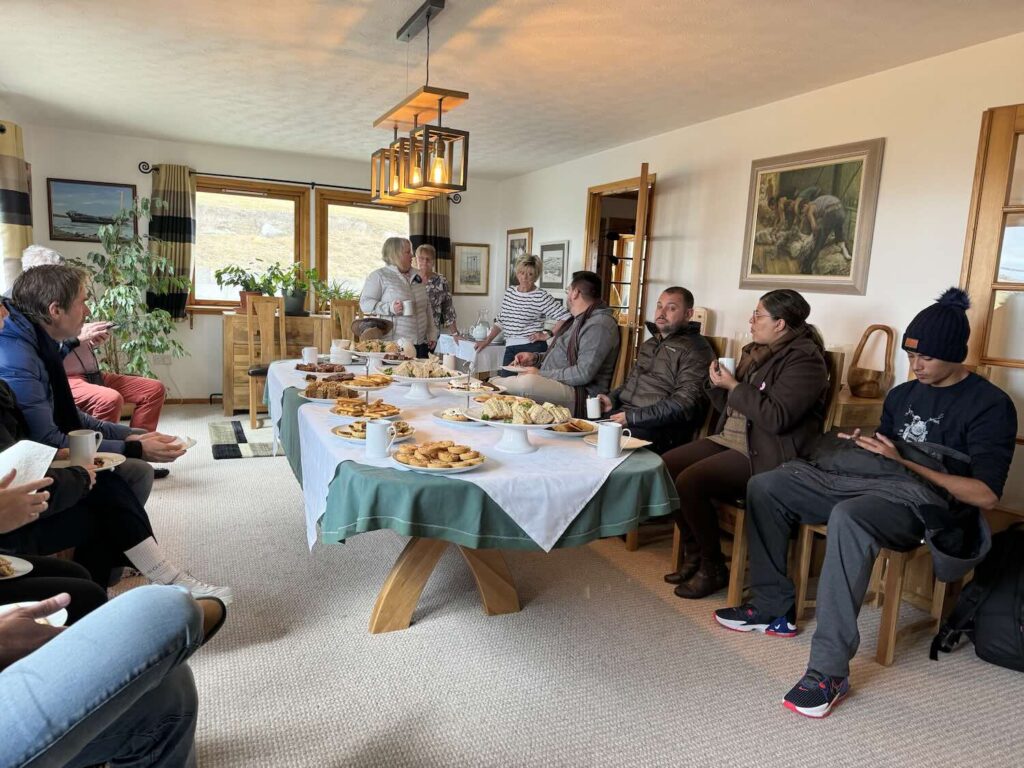 mesa com diversas comidas e pessoas ao redor.