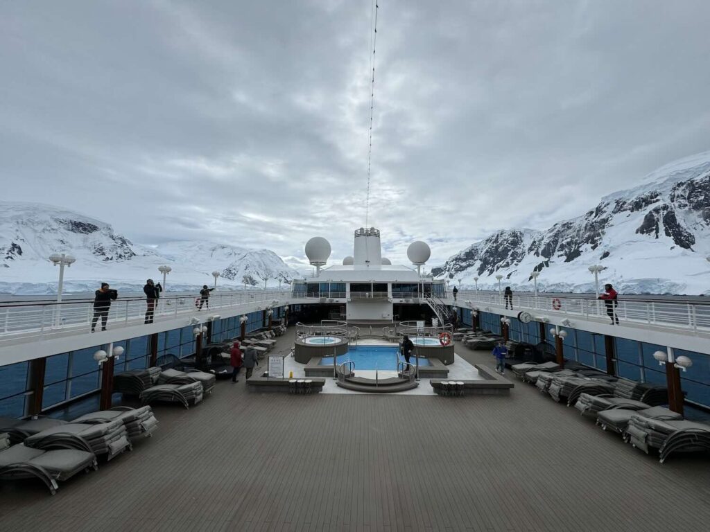 deck de navio com piscina e montanhas da antártida ao fundo.