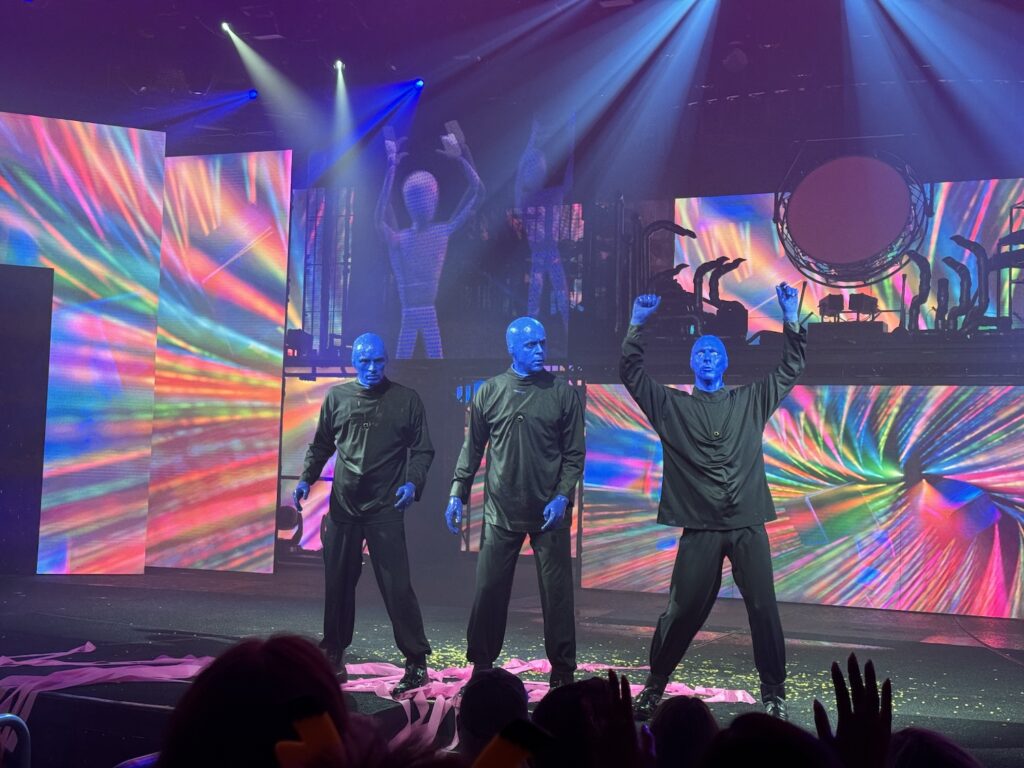 3 homens vestidos de preto e com o rosto pintados de azul