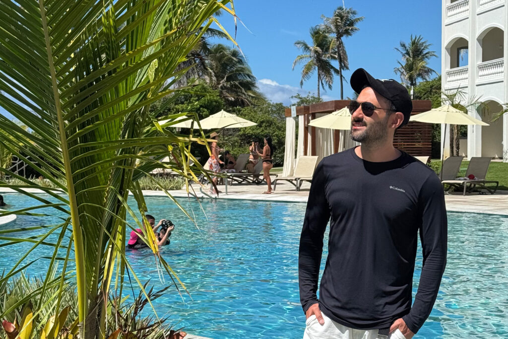 homem em frente a piscina,com camisa de manga longa preta, boné preto e bermuda branca