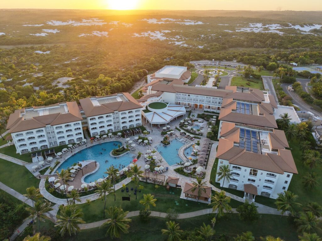 imagem de drone de estrutura de um resort com destaque poara as piscinas e pôr do sol ao fundo