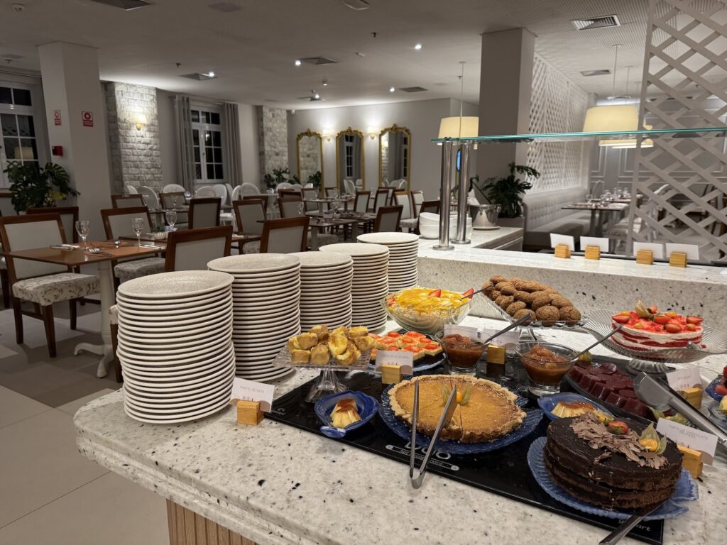 buffet de doces e ao fundo diversas mesas e cadeiras de um restaurante de hotel