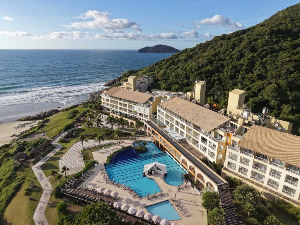 imagem aérea de um resort encostado em um morro e de frente para o mar. 