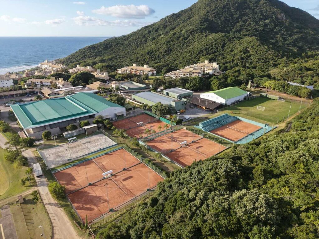 imagem aérea de quadras de areia em um resort encostado no morro e de frente para o mar